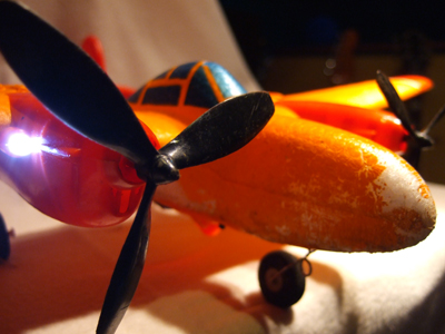 Die orange P-38 Lighting von Air Ace, die darauf in meinen kleinen Hobby-Hangar geliefert wurde, kann ich jedoch unbedingt empfehlen. Aufladen, losfliegen und Spaß haben. Loslegen sollte man zunächst mit dem mitgelieferten Akku incl. Ladegerät in der Fernsteuerung- 10 Minuten Flugzeit pro austauschbarem NiCd Akku sind allemal drin, aber sollte man auch hier auf ein ruhiges Lüftchen achten, sonst kann man sich schon mal auf längere Fußmärsche durch den Acker einstellen. Ideal auch hier die Zeit vor Sonnenuntergang- als besonderen Gag hat der Flieger 3 helle LEDs eingebaut, die sich im fast Dunkel schon als hilfreich zur Ermittlung der Flugrichtung oder Absturzstelle erwiesen haben. A propos Abstürze: Davon hat die P-38 in Anfangszeiten mehr abbekommen, als ich hier auflisten könnte. Autos, Bäume, senkrecht in den Boden, an Hauswände und in Zäune- es gab bisher kein ungewolltes Zielgebiet, das der Flieger nicht verkraftet hätte. Bricht doch mal was ab: hier hilft Tesafilm oder EPP Kleber und schon kann's weitergehen.